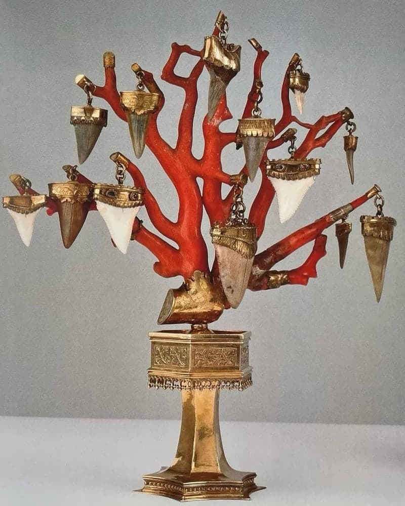 A branch-coral tree hung with gold-collared shark teeth, on a gilt pedestal.